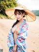 A woman in a blue kimono and a straw hat on the beach.