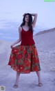 A woman in a red tank top and a floral skirt.