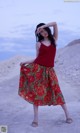 A woman in a red top and a floral skirt posing for a picture.