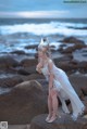 A woman in a white dress standing on a rock by the ocean.