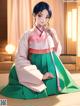 A woman in a green and pink hanbok sitting on the floor.