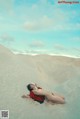 A naked woman laying on top of a sand dune.