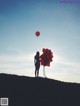 A woman standing on top of a hill holding a bunch of red balloons.