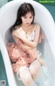 A woman sitting in a bathtub in a pink dress.