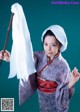 A woman in a kimono holding a white cloth and a stick.