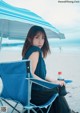 A woman sitting in a chair under an umbrella on the beach.