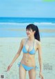 A woman in a blue bikini standing on a beach.